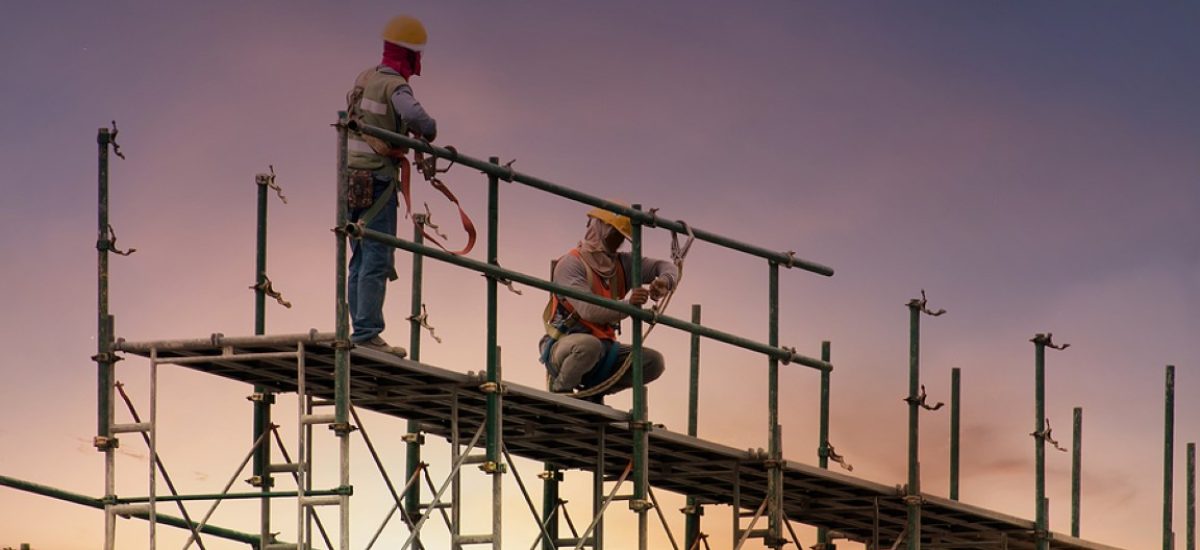 Man Working On Construction Site With Scaffold And Building With